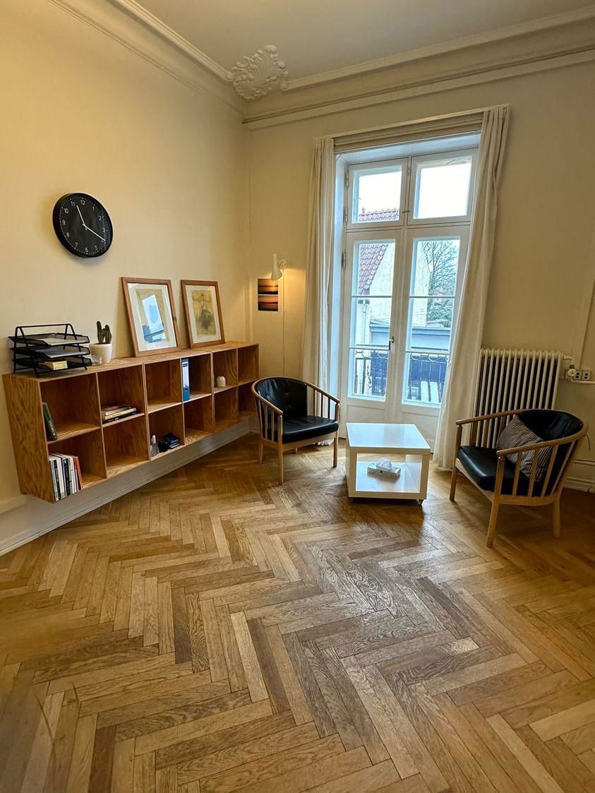 Et rummeligt lokale til samtale, hvor man ser et bord, to stole og reoler