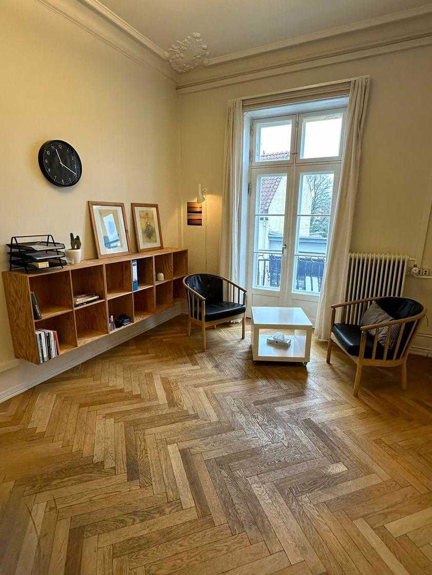 Et rummeligt lokale til samtale, hvor man ser et bord, to stole og reoler